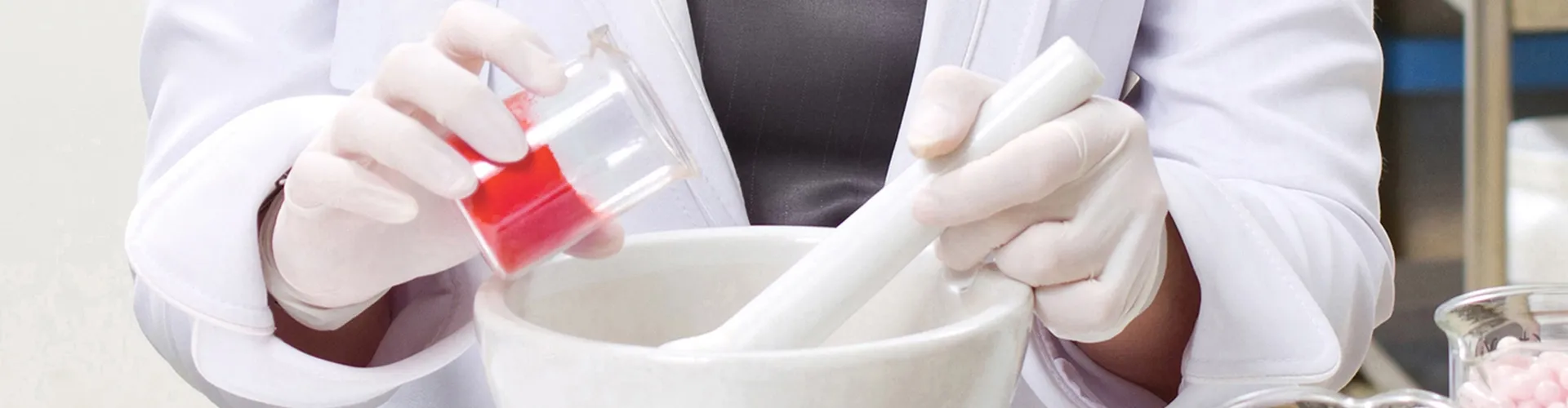 Arzneimittelherstellung. Rote Substanz wird mit einer Hand einem Gefäß hinzugefügt. In der anderen Hand ein Stößel